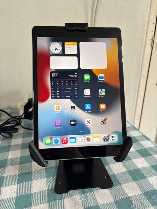 An iPad held in a black security case, standing upright on a table using its flip-out stand.